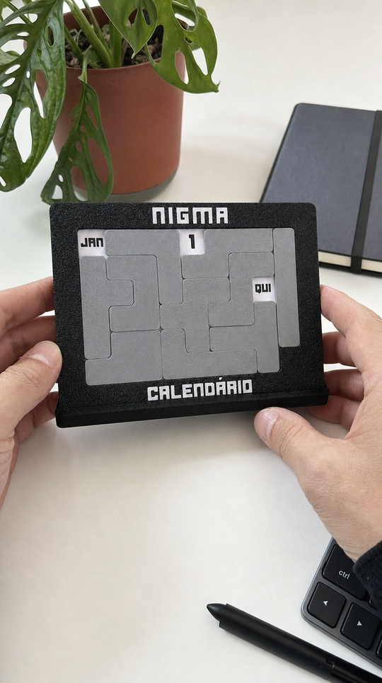 Calendário Nigma J7 nas mãos, mesa branca com monstera (imagem ilustrativa)