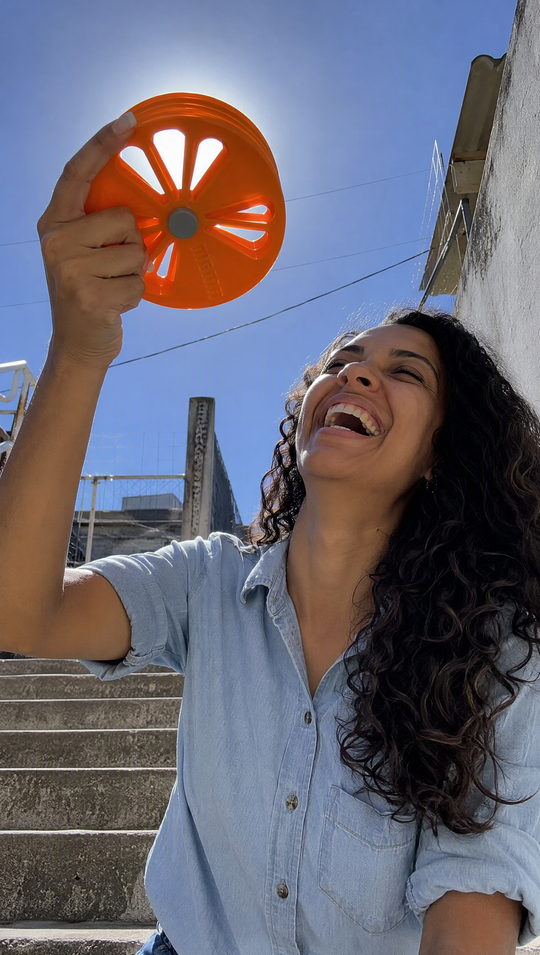 Mulher rindo com o Nigma P5 erguido contra o sol, luz atravessando só os vãos alinhados